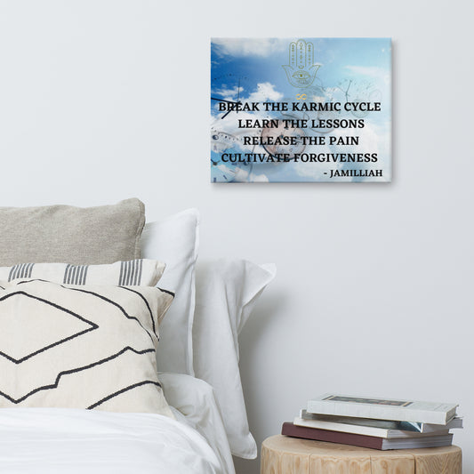 16x20 textured canvas print with original logo and slogan/saying. Wall art with clocks in the blue, clouded sky with hamsa hand/infinity sign brand logo, and black printed, unique, wise quote mantra/tagline/motto. "Break The Karmic Cycle, Learn The Lessons, Release The Pain, Cultivate Forgiveness." - Jamilliah - Shown on wall above bed/pillows and next to stand with books. JAMILLIAH'S WISDOM IS TIMELESS SHOP - wisdomistimeless.com.