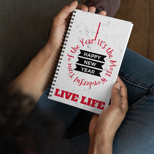 Metal wire-o binding/spiral diary/notepad/notebook. Gray-white cover with gray-black speckles, front view. Wise quotes/mantras/mottos/sayings/taglines. "It's the Most Wonderful Time of the Year," "Live Life," (red) and "Happy New Year" (black and white.) 140 dotted pages. 5.5 inches x 8.5 inches. Shown in the hands of a model wearing blue jeans. Jamilliah's Wisdom Is Timeless Shop - wisdomistimeless.com.