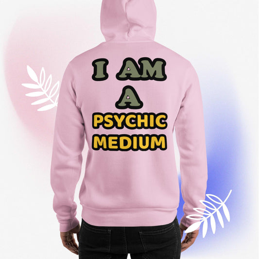 Light pink, unisex, heavy blend, hoodie, back view. Hoodies with messages on the back. Graphic hoodies with quotes. Hoodies with text on back. Otherworldly, supernatural quote, in mixed colored writing of olive green and mustard yellow, outlined in black. "I Am A Psychic Medium." Worn by male model, surrounded by white leaves, and pink and blue hues. JAMILLIAH'S WISDOM IS TIMELESS SHOP - wisdomistimeless.com.