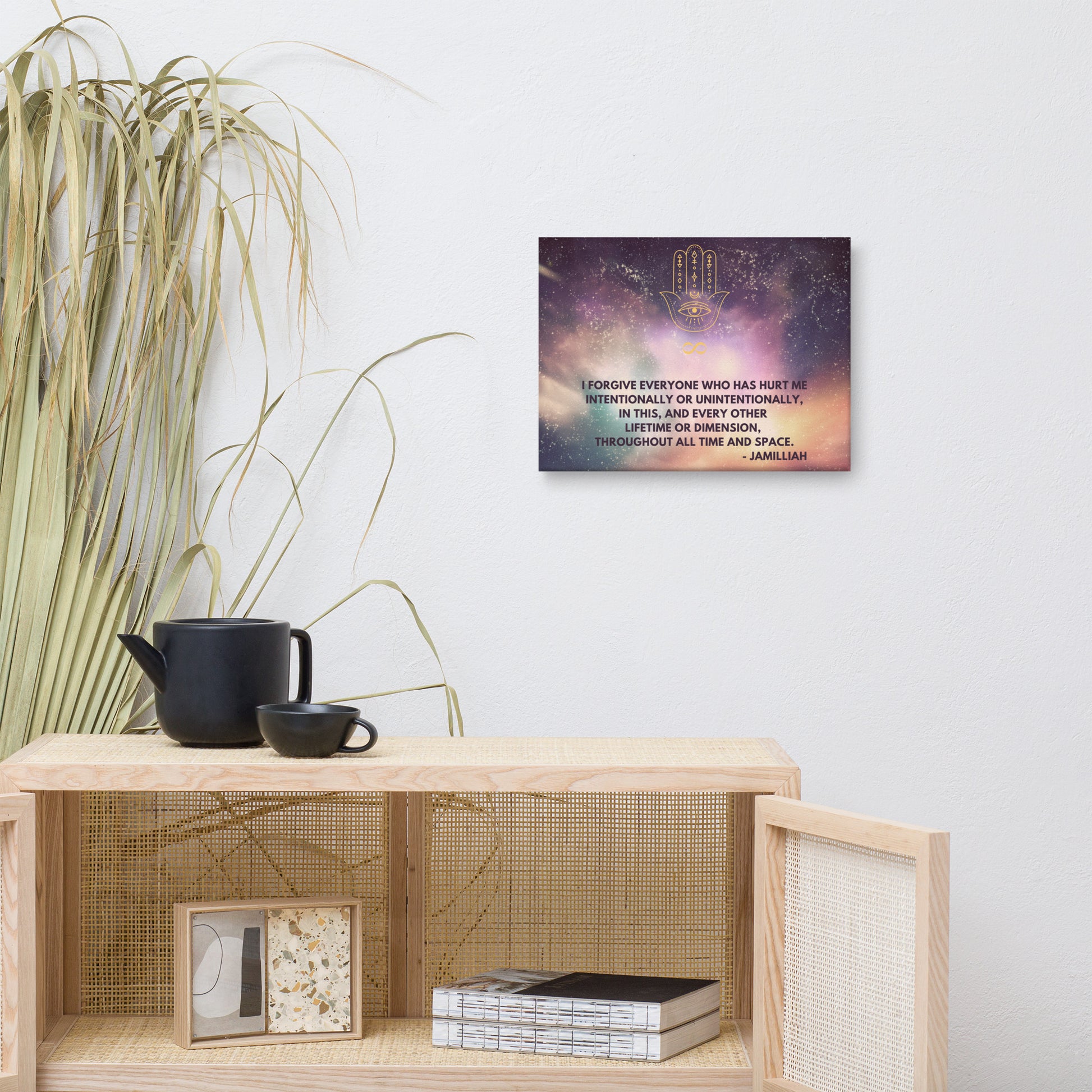 12x16 inch, semi-gloss/textured/fade resistant canvas print. Purple/green/yellow space/universe/cosmos design with spiritual hamsa hand/infinity symbol/sign brand logo image, and original wise quote mantra/saying/tagline/motto/slogan. "I Forgive Everyone Who Has Hurt Me Intentionally Or Unintentionally, In This, And Every Other Lifetime Or Dimension, Throughout All Time And Space. - Jamilliah." Shown on wall next to plant, cabinet, mug, and teapot. JAMILLIAH'S WISDOM IS TIMELESS SHOP - wisdomistimeless.com.