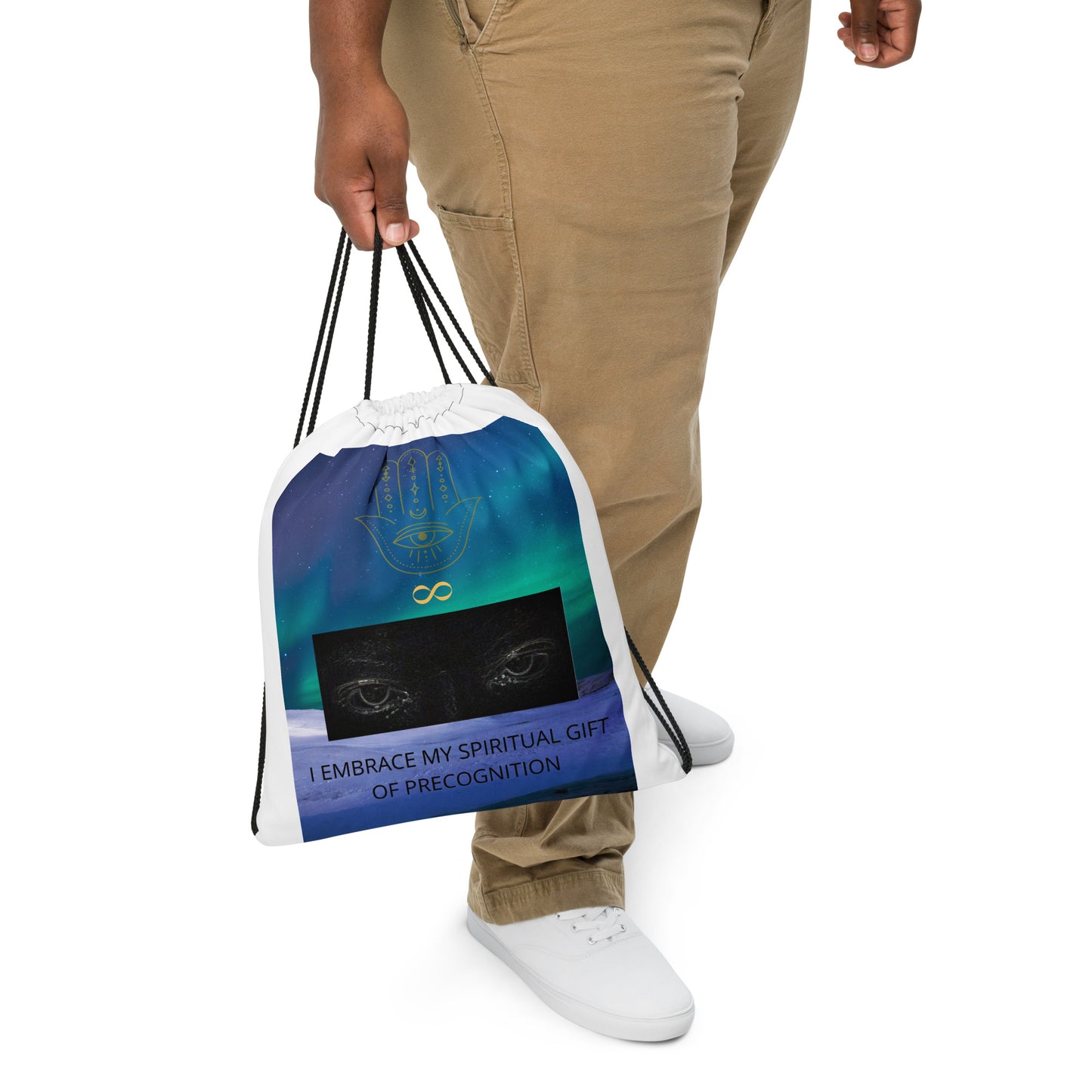 White bag with black drawstrings. Colorful bluish/greenish sky design of polar lights/aurora borealis. Green hamsa hand and yellow infinity symbol logo. Grayish/white outline of a pair of eyes. Other-worldly, supernatural, paranormal tagline "I Embrace My Spiritual Gift Of Precognition." Shown hanging down from model's hand, white background. JAMILLIAH'S WISDOM IS TIMELESS SHOP - wisdomistimeless.com.
