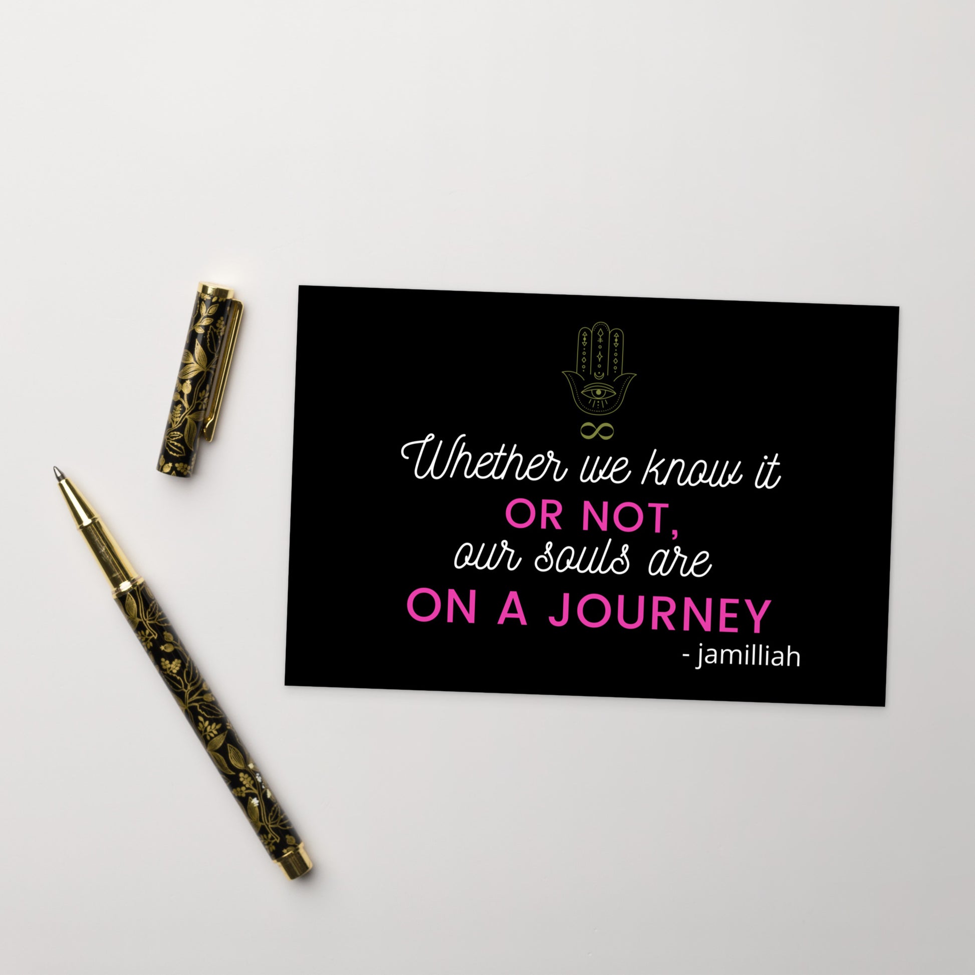 4" x 6", black, glossy, cardboard postcard with pink and white writing, original hamsa hand/infinity symbol brand logo, and wise quote mantra/saying/motto/tagline. "Whether We Know It Or Not, Our Souls Are On A Journey" - Jamilliah. Slogan is "JAMILLIAH'S THE SOUL-PATH JOURNEY PODCAST" tagline. Shown with fancy pen and cap. JAMILLIAH'S WISDOM IS TIMELESS SHOP - wisdomistimeless.com.