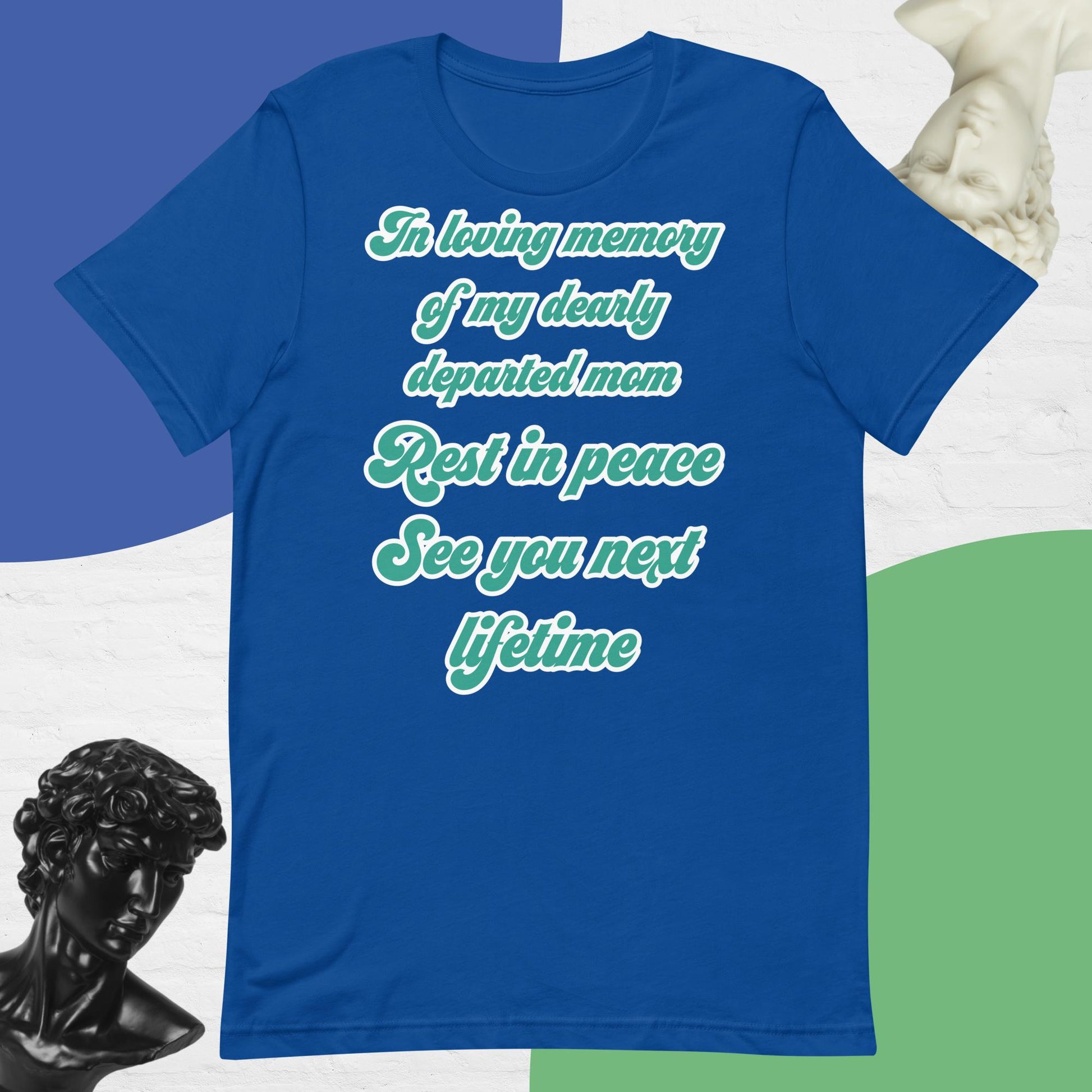 Bella + Canvas 3001 t-shirt. True royal blue colored, front view. White, green, and black scripted written quote "In loving memory of my dearly departed mom. Rest in peace. See you next lifetime." Shown laying flat on a white, green, and blue background with black and white bust sculptures of people's head and necks. Jamilliah's Wisdom Is Timeless Shop - wisdomistimeless.com.