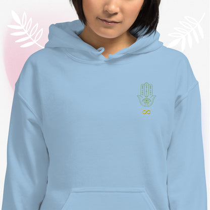Light blue, unisex, heavy blend, hoodie, front. Embroidered, otherworldly, supernatural, hamsa hand/infinity symbol logo. Worn by female model, surrounded by white leaves, and pink hue. JAMILLIAH'S WISDOM IS TIMELESS SHOP - wisdomistimeless.com.