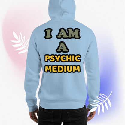 Light blue, unisex, heavy blend, hoodie, back. Otherworldly, supernatural quote, in mixed colored writing of olive green, mustard yellow, outlined in black. "I Am A Psychic Medium." Worn by male model with hood down, and surrounded by white leaves with pink and blue hues. JAMILLIAH'S WISDOM IS TIMELESS SHOP - wisdomistimeless.com.