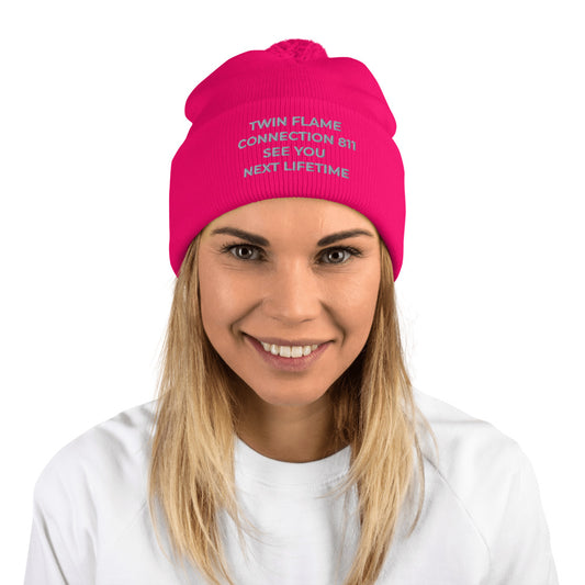 Neon pink and grey pom-pom knit cap with original tagline. "Twin Flame Connection 811 See You Next Lifetime." Shown on female model. JAMILLIAH'S WISDOM IS TIMELESS SHOP - wisdomistimeless.com.