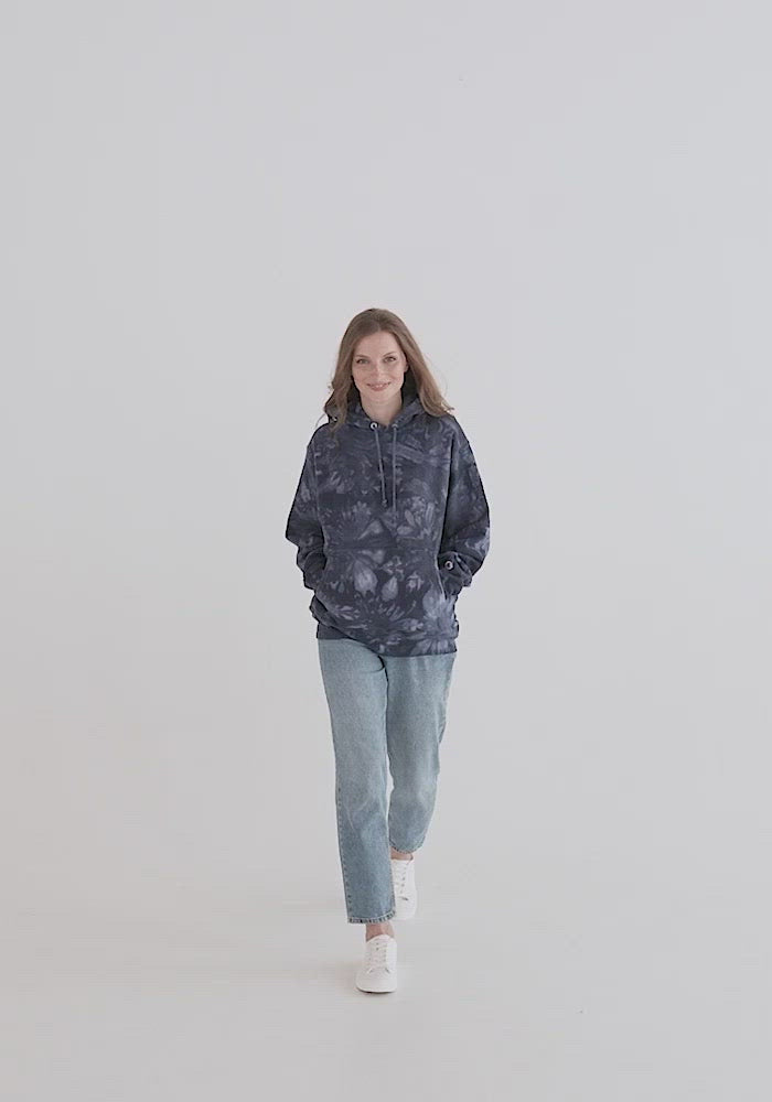 Unisex navy Champion tie-dye hoodie, live video with male and female models. Product detail of hood, drawstrings, sleeves, logo, and fit. Two-ply hood with matching drawcords, front pouch pocket, and embroidered "C" Champion logo on left sleeve. 1×1 rib knit side panels, sleeve cuffs, and bottom hem. Sizes small, medium, large, and extra large. JAMILLIAH'S WISDOM IS TIMELESS SHOP - wisdomistimeless.com.